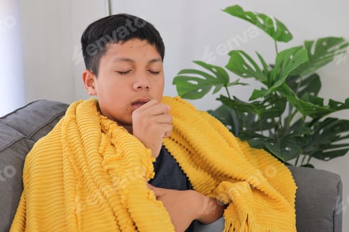 Preview: Sick Young Asian Boy in Cozy Blanket Resting on a Couch with Severe Cough