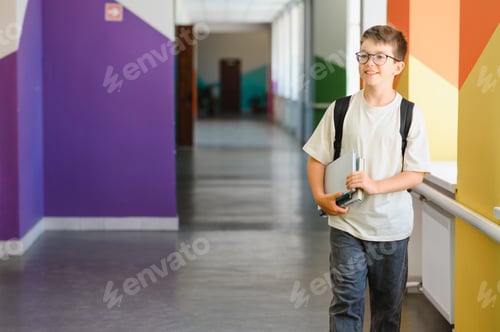 Preview: Smiling pupil walking in school hallway carrying books and laptop