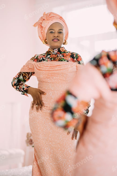 Preview: Playful charming African lady in elegant trendy pink dress with ethnic print, traditional headwrap