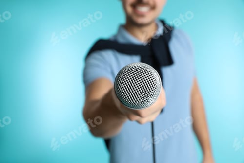 Preview: Young handsome man in casual clothes holding microphone on color background, closeup