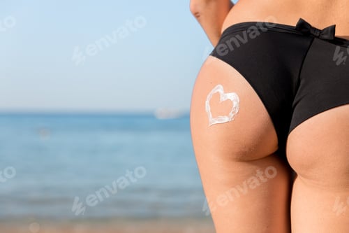 Preview: Heart shape made of sun cream on a woman buttocks over the sea background