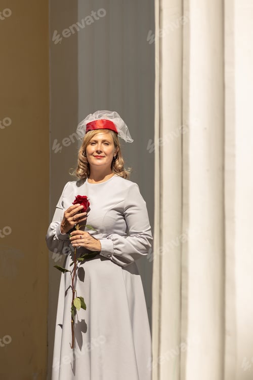 Preview: Young woman in vintage red hat and retro blue dress walking in summer park.