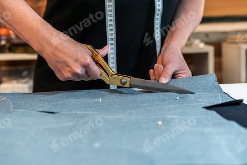 Preview: Seamstress using scissors to cut textile at work table.