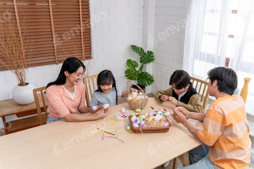 Preview: Asian young children and parents coloring Easter eggs on table in house.