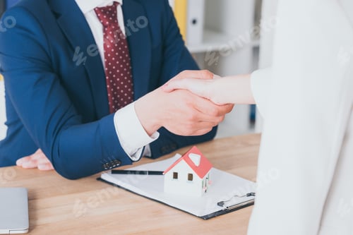 Preview: partial view of customer shaking hands with realtor near house model