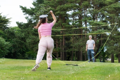 Preview: Focus on young woman with racket playing badminton with man in the park. Friends having fun