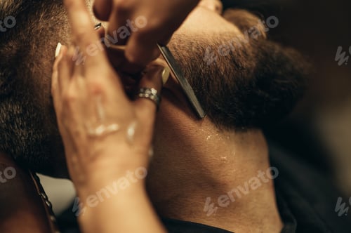 Preview: Man getting shaved with straight edge razor by hairdresser at barbershop
