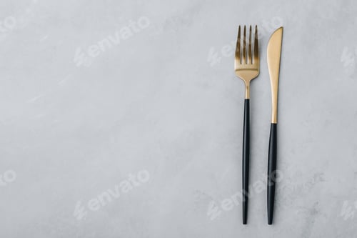 Preview: Gold fork and knife on gray stone background, top view