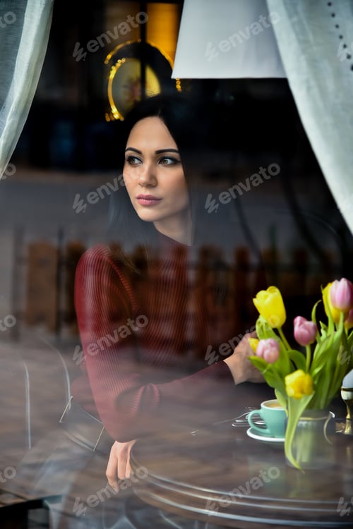 Preview: A young beautiful girl looks at the street from the window of a cafe.
