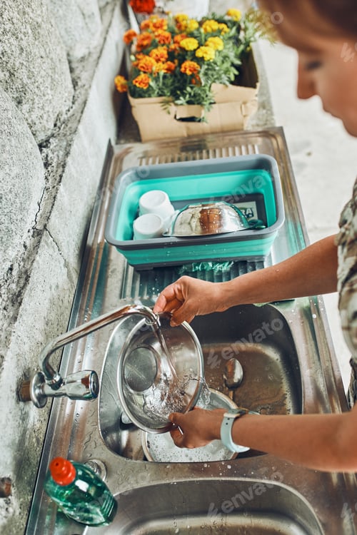 Preview: Woman washing up the dishes pots and plates in the outdoor kitchen during vacations on camping.