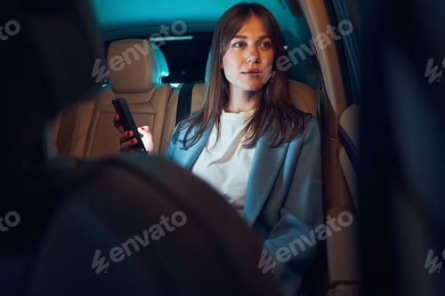 Preview: Businesswoman with mobile phone riding in car