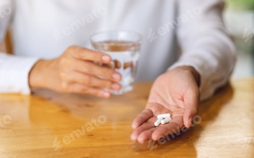 Preview: Closeup image of a woman holding white pills and a glass of water