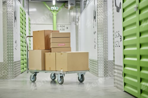 Preview: Stacked Cardboard Boxes on Trolley Standing in Self Storage Facility Corridor
