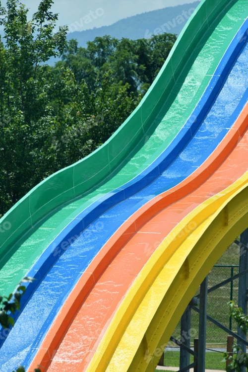 Preview: Rainbow water slide at an outdoor water park amusement park. green blue orange yellow stripes