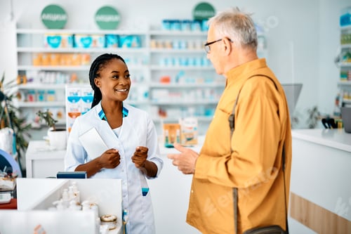 Preview: Happy African American pharmacist talking to senior man in a pharmacy.