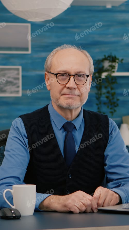 Preview: Elderly businessman entrepreneur sitting in workspace looking at camera