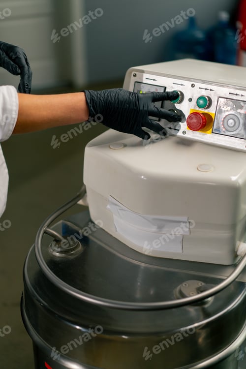 Preview: close-up of a woman's hand pressing the power button on a kitchen planetary mixer for mixing dough