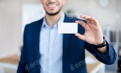 Preview: Cropped view of young Arab man showing empty business card with mockup for design at modern office