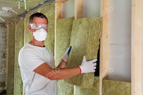 Preview: Worker in protective goggles and respirator insulating rock wool insulation
