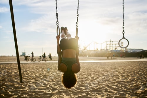 Preview: fit african american woman flipping upside down on gymnastic rings at exercise park