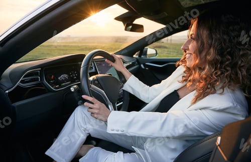 Preview: Cheerful woman sitting in car during sunset.