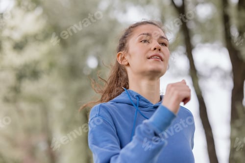 Preview: portrait of a woman in a blue hoodie. jogging in the park. a European athletic woman is running