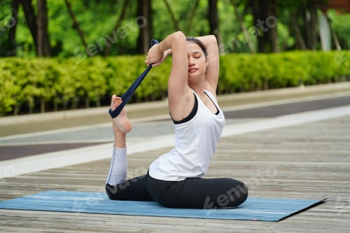 Preview: Attractive young woman in sports clothing practicing yoga balance at park.