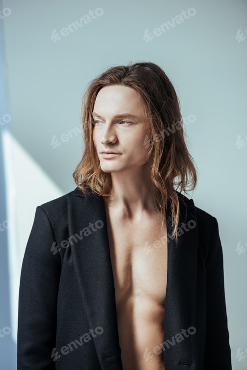 Preview: handsome shirtless man with long hair posing in black jacket, on grey