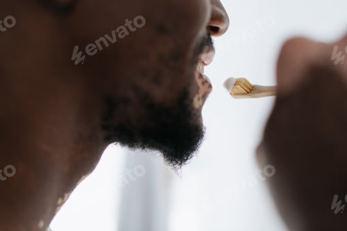 Preview: Cropped view of african american man with vitiligo brushing teeth at home