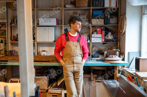 Preview: Relaxed dreaming man carpenter smiling looks out of window taking break lounging at joiner workshop.