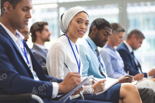 Preview: Smiling young businesswoman while writing notes during seminar in office building