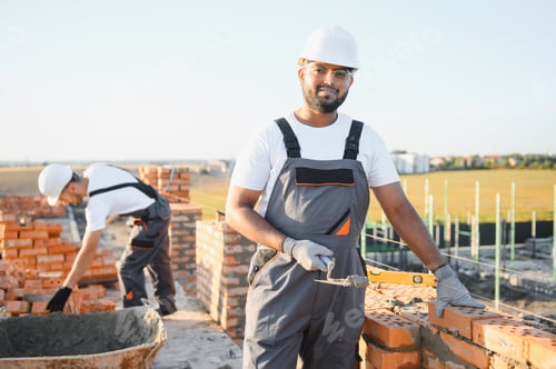 Preview: A team of Indian construction workers in overalls and hard hats are building a brick wall