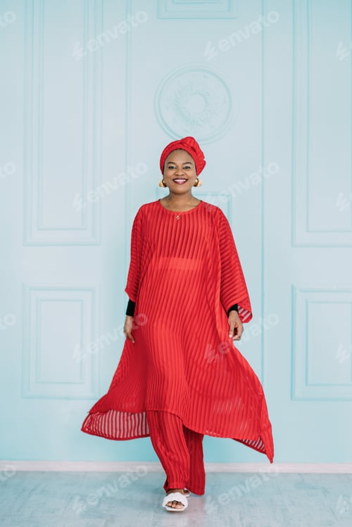 Preview: Full length portrait of smiling African woman dressed in stylish traditional ethnic red suit and