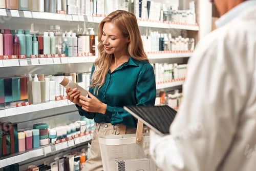 Preview: Woman examining cosmetic product in pharmacy aisle