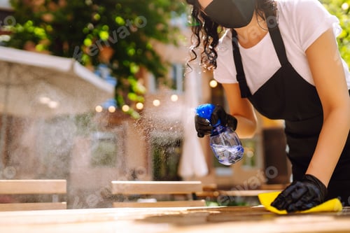 Preview: Disinfecting to prevent COVID-19. Young waitress cleaning table with disinfectant spray.