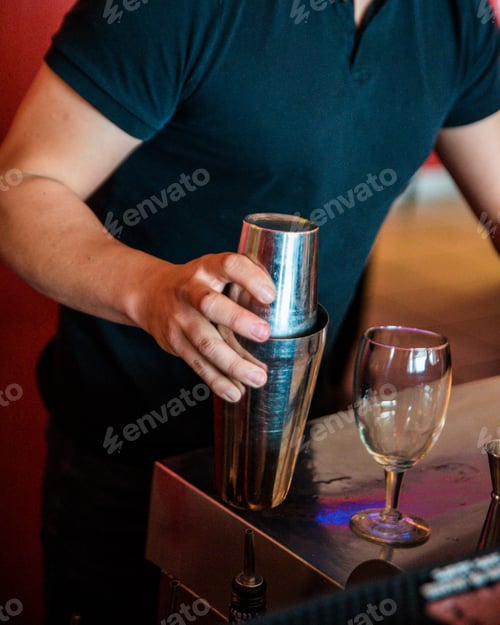 Preview: Vertical shot of a bartender in black mixing a cocktail in metal cups