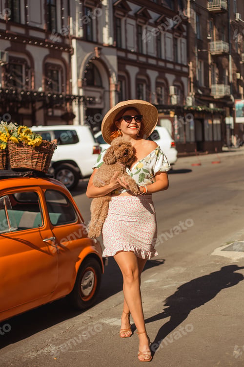 Preview: A young beautiful woman in sunglasses and hat walks around the city on a summer day holding her pupp