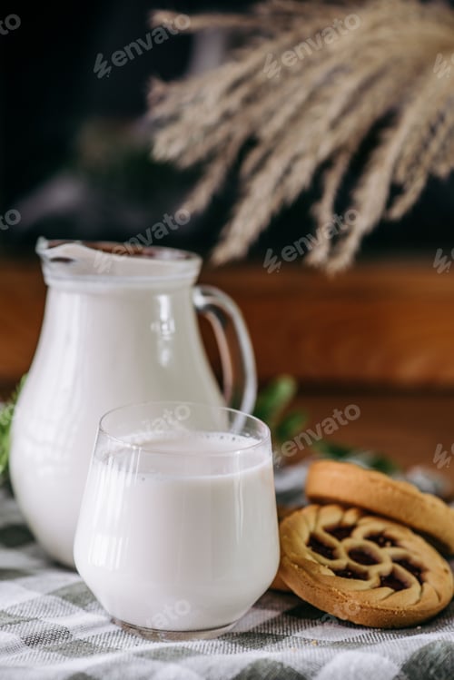 Preview: Jug of milk on a wooden table alongside a plate of freshly baked cookies