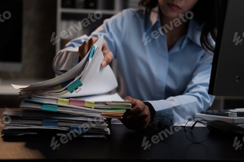 Preview: Young adorable Asian businesswoman working with work document during the night, working overtime at