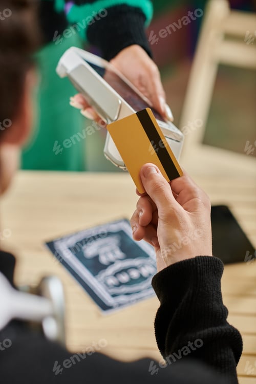 Preview: customer holding credit card near contactless card reader, cropped hand of man paying in vegan cafe