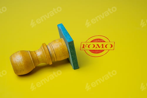 Preview: A close-up image of a wooden stamp with a red "FOMO" imprint on a yellow background.