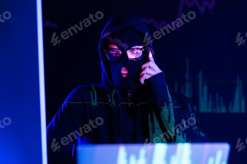 Preview: Pensive hacker in balaclava looking at laptop on black background with charts reflection