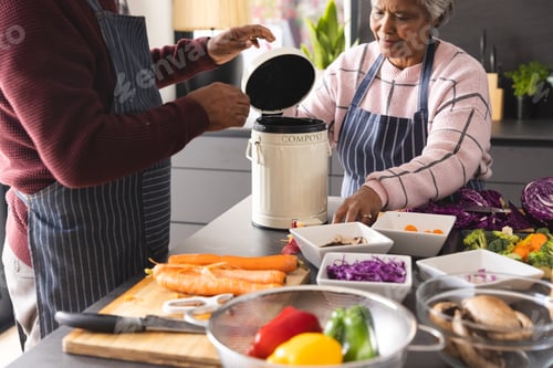 Preview: Senior biracial couple wearing aprons composting food waste in kitchen at home