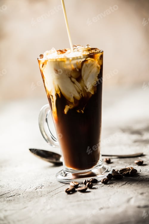 Preview: Ice coffee in a tall glass with cream poured over and coffee bea