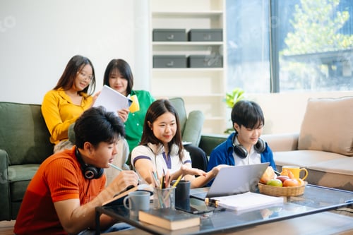 Preview: Group of young Asian students working on a project with laptops and tablets. Cozy indoor setting,