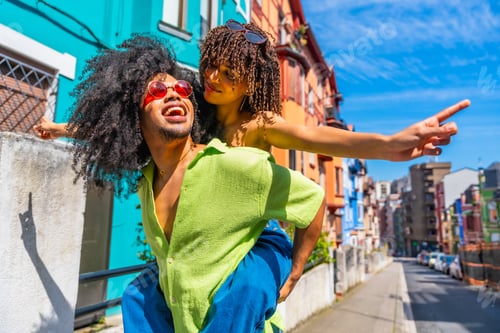 Preview: Young couple piggybacking and pointing in colorful city street
