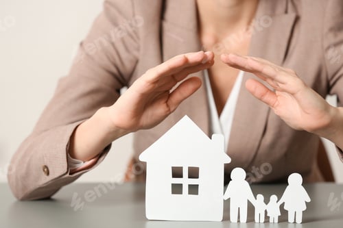 Preview: Female agent covering house model and family at table, closeup. Home insurance