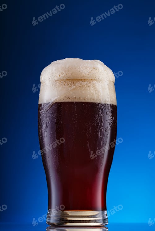 Vista previa: Glass of dark beer with foam on blue background