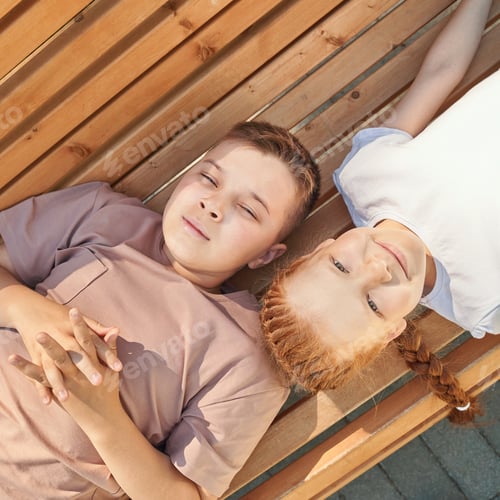Preview: Caucasian children relaxing on wooden bench in sunlight smiling and enjoying
