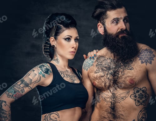 Preview: Portrait of shirtless, tattooed bearded male and brunette female with tattoo ink on her torso.